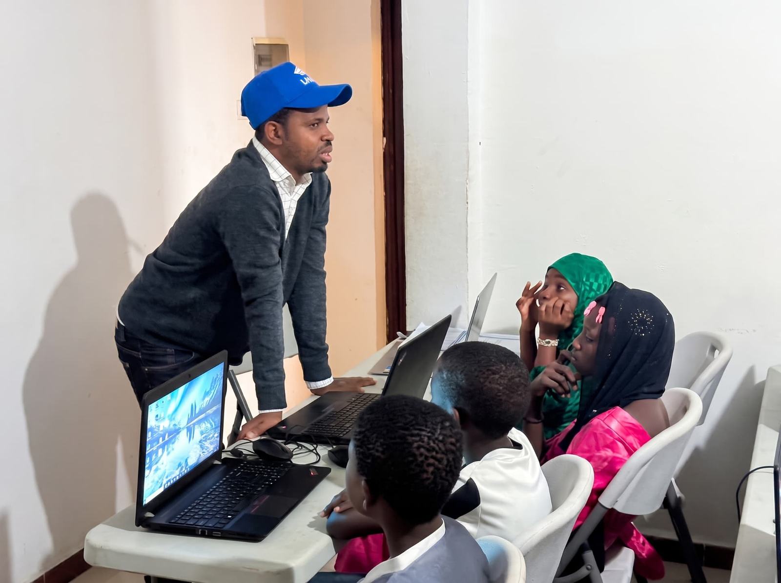 A facilitator supports young learners seated together with laptops during a practical digital skills session.