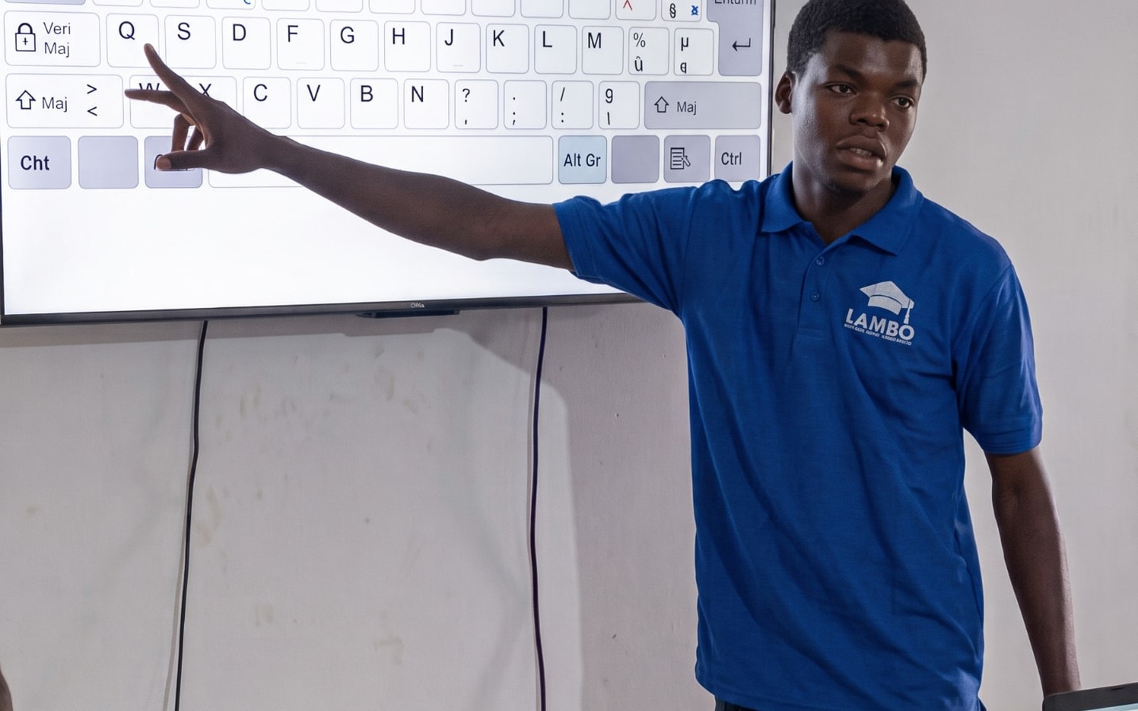 A facilitator teaching keyboard skills on a large display during an in-person class in coastal West Africa