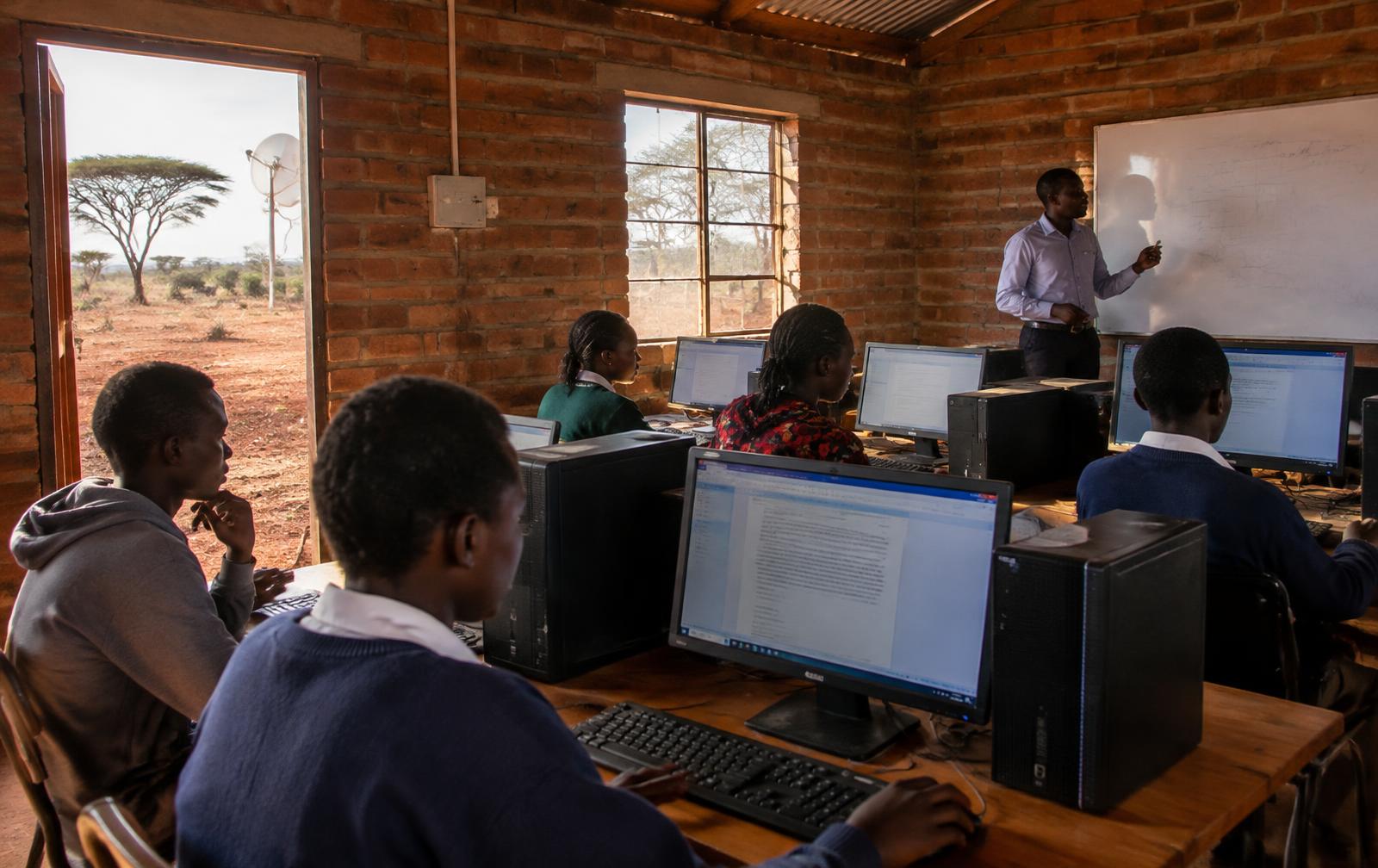 A facilitator teaching students at desktop computers in a rural learning center in East Africa
