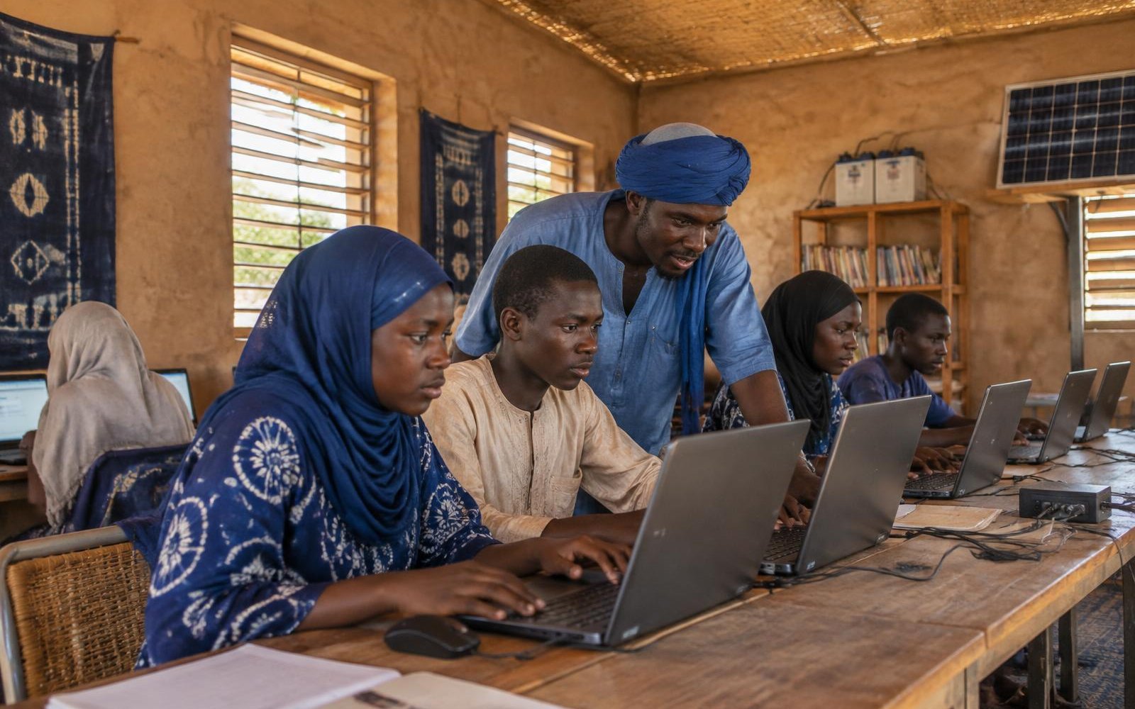 Young people learning on solar-powered laptops with a facilitator in a Sahel community center