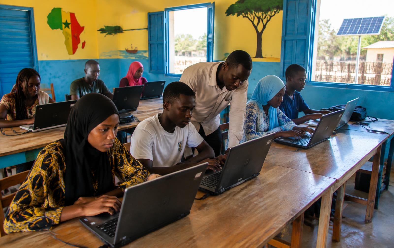 Students learning on laptops in a colourful community classroom in West Africa